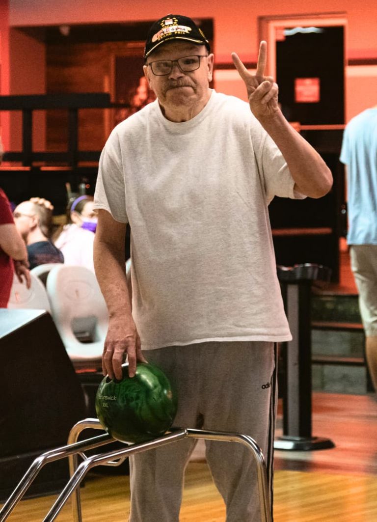 a man giving a peace sign and holding a bowling ball at the bowling alley